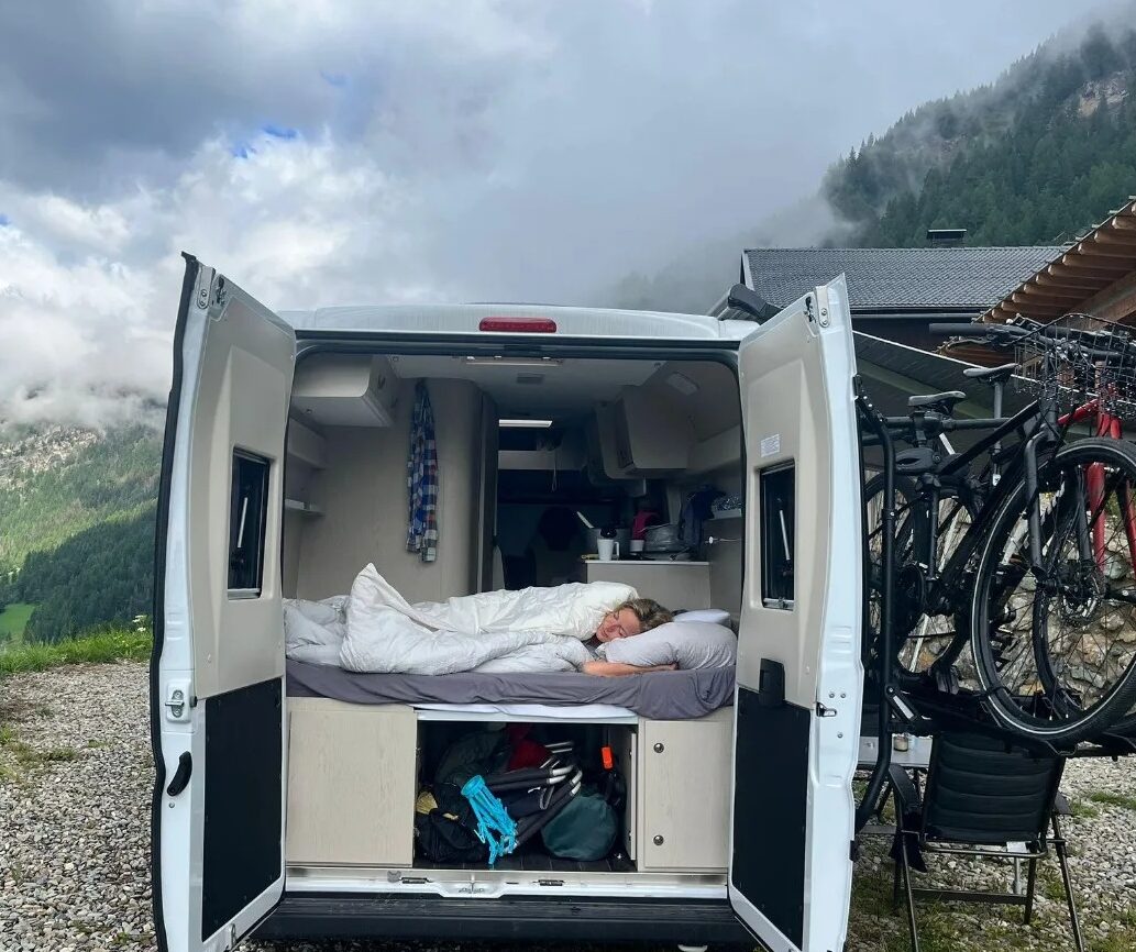 Neu vs Gebraucht Campervan Lifestyle Reisender ruht sich in einem Campervan aus, der in den Bergen geparkt ist.