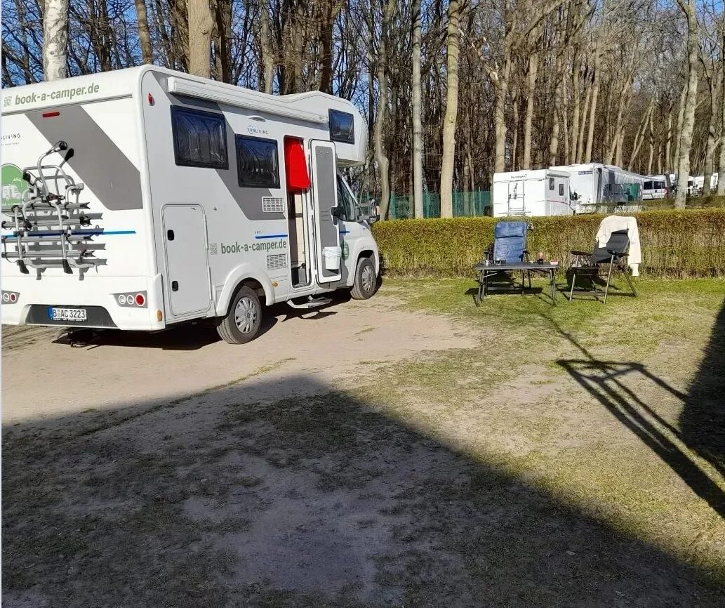 Ein geparkter Wohnmobil auf einem Campingplatz mit im Freien aufgestellten Stühlen und einem Tisch, der die effiziente Nutzung von Campervan-Strom für Outdoor-Aktivitäten zeigt.